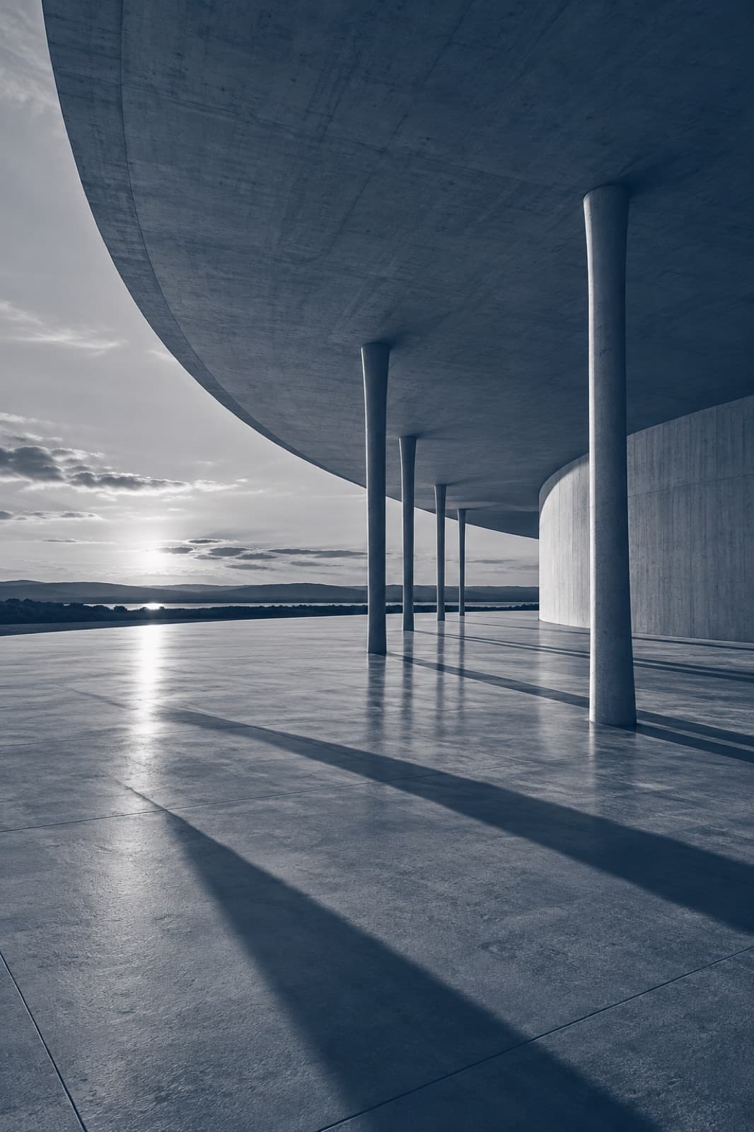 Marquise de concreto sobre pilotis com sombras de fim de tarde, em tons de azul