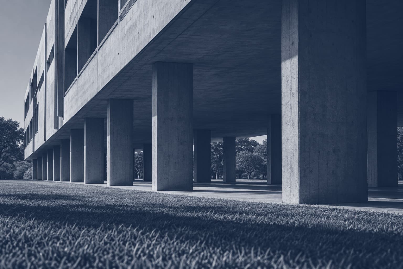 Prédio modernista de concreto erguido sobre pilotis, visto do gramado, em tons de azul