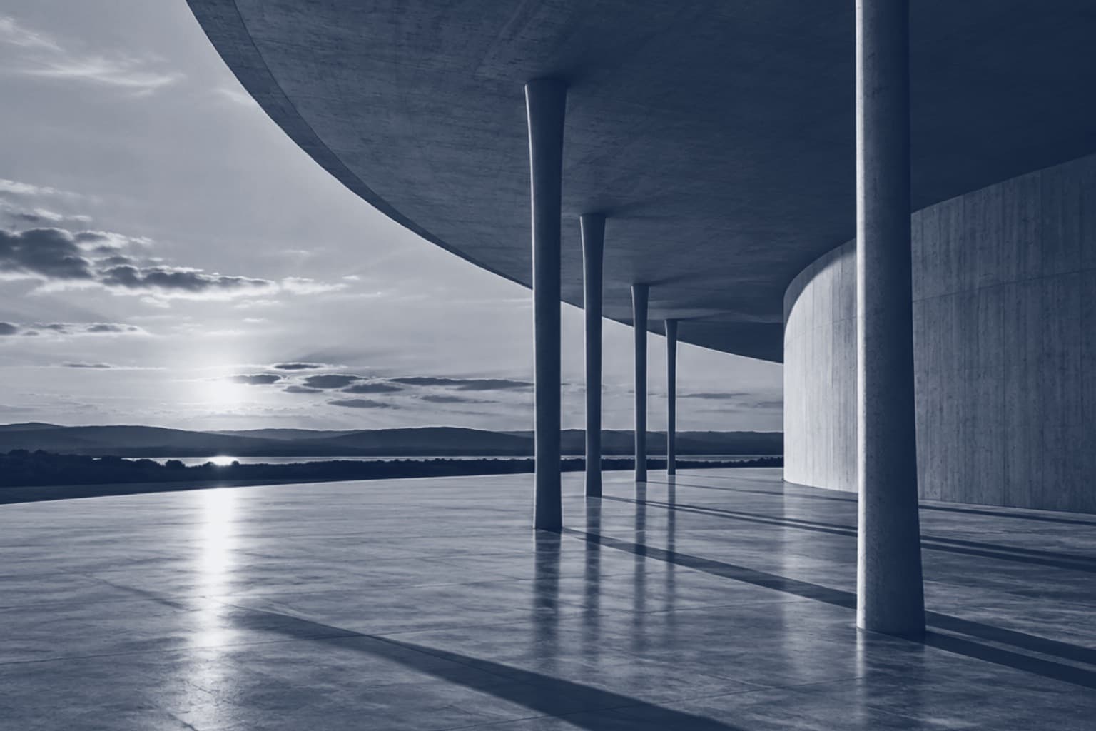 Marquise curva de concreto sobre colunas finas, com o sol baixo refletido no piso, em tons de azul